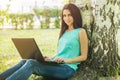 Woman sitting on grass, using laptop and typing