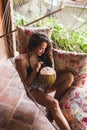 Woman sitting in hammock with colorful pillows and drinking fresh young coconut Royalty Free Stock Photo