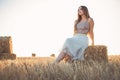 Woman sitting on hay stack walking in summer evening, beautiful romantic girl with long hair outdoors in field at sunset Royalty Free Stock Photo
