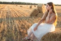 woman sitting on hay stack walking in summer evening, beautiful romantic girl with long hair outdoors in field at sunset Royalty Free Stock Photo