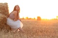 Woman sitting on hay stack walking in summer evening, beautiful romantic girl with long hair outdoors in field at sunset Royalty Free Stock Photo