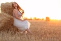 Woman sitting on hay stack walking in summer evening, beautiful romantic girl with long hair outdoors in field at sunset Royalty Free Stock Photo