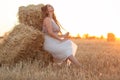 Woman sitting on hay stack walking in summer evening, beautiful romantic girl with long hair outdoors in field at sunset Royalty Free Stock Photo