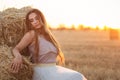 Woman sitting on hay stack walking in summer evening, beautiful romantic girl with long hair outdoors in field at sunset Royalty Free Stock Photo