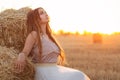 Woman sitting on hay stack walking in summer evening, beautiful romantic girl with long hair outdoors in field at sunset Royalty Free Stock Photo