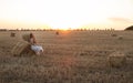 Woman sitting on hay stack walking in summer evening, beautiful romantic girl with long hair outdoors in field at sunset Royalty Free Stock Photo