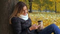 Woman Sitting With Her Back To The Tree In Yellow Autumn Leaves, Uses Smartphone Royalty Free Stock Photo