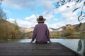 Woman sitting with her back on a wooden bridge looks to the future with a beautiful view of a mountain lake and forest Royalty Free Stock Photo