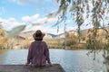 Woman sitting with her back on a wooden bridge looks to the future with a beautiful view of a mountain lake and forest Royalty Free Stock Photo