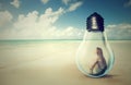 Woman sitting inside a light bulb on a beach looking at the ocean view Royalty Free Stock Photo