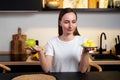 Woman sitting in the kitchen, choosing between a sweet cake and an apple. Royalty Free Stock Photo