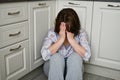 Woman is sitting on kitchen floor covering her face with her hands. Depression, grief or frustration