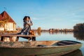 Woman sitting on lake pier by boat admiring autumn landscape. Fall season activities Royalty Free Stock Photo