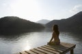 Woman Sitting On Lakeside Jetty At Dawn