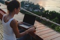 Woman sitting with a laptop and a cup of coffee in front of sunset view