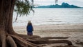 Woman sitting on large tree roots on the beach looking at her phone