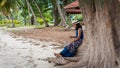 Woman sitting on large tree roots on the beach looking at her phone