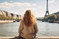 Woman Sitting on Ledge, Looking at Eiffel Tower, Young traveler woman rear view sitting on the quay of Seine River looking at the