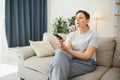 Woman sitting in living room holding remote control smiling. Royalty Free Stock Photo