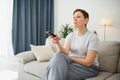 Woman sitting in living room holding remote control smiling. Royalty Free Stock Photo