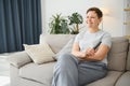 Woman sitting in living room holding remote control smiling. Royalty Free Stock Photo