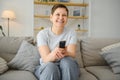 Woman sitting in living room holding remote control smiling. Royalty Free Stock Photo