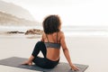 Woman sitting on a mat on beach at sunset. Back view of a female relaxing after yoga exercises Royalty Free Stock Photo