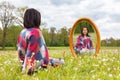 Woman sitting with mirror in blooming meadow