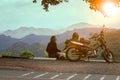 woman sitting beside motorcycle at beautiful viewpoint and looking to sunset scene
