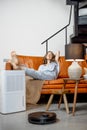 Woman sitting near air purifier and robotic vacuum cleaner