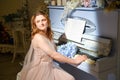 A woman is sitting near a vintage piano with a blue bouquet of flowers. Studio portrait of musician woman in pink dress