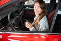 Woman sitting in new red car holding key rejoicing her purchase in dealership Royalty Free Stock Photo