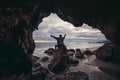 Woman sitting on the ocean rocks cave with arms raised and enjoy the nature and freedom