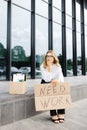 Woman sitting outdoor with cardboard banner with the slogan Need work next to box of stuff. Beautiful female protester at strike Royalty Free Stock Photo