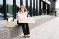 Woman sitting outdoor with poster Act Now next to box of stuff . Beautiful female protester at strike against unemployment Royalty Free Stock Photo