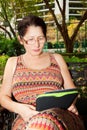 Woman sitting on a park bench and reading e-book Royalty Free Stock Photo