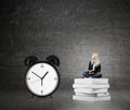 Woman sitting on pile of books, big alarm clock right Royalty Free Stock Photo