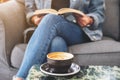 A woman sitting and reading a vintage novel book on sofa with coffee cup on the table