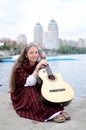 Woman sitting on the river bank with guitar in traditional scottish clothes