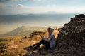 A woman sitting on rocky mountain using smartphone and looking out at beautiful natural view Royalty Free Stock Photo