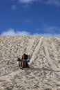 Woman sitting on the sand, joyfully sliding down a small hillside in Lancelin Sand Dunes, Australia