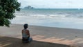 Woman sitting on sidewalk at beach looking at islands