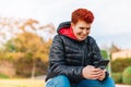 Close-up of a modern woman with short red hair, non-binary, looking at her social networks in a public park.