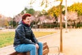 Modern non-binary woman with short red hair, happy, sitting in a public park.