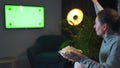 Woman sitting on a sofa in the living room in the evening and watching a green TV screen mockup, is emotionally worried