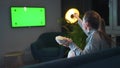 Woman sitting on a sofa in the living room in the evening and watching a green TV screen mockup, is emotionally worried
