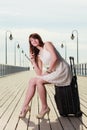 Woman sitting on suitcase, pier in background