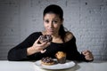 Woman sitting at table feeling guilty forgetting diet eating dish full of junk sugary unhealthy food Royalty Free Stock Photo