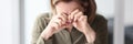 A woman sitting at a table in the office wipes her eyes