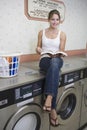 Woman Sitting On Washing Machine At Launderette